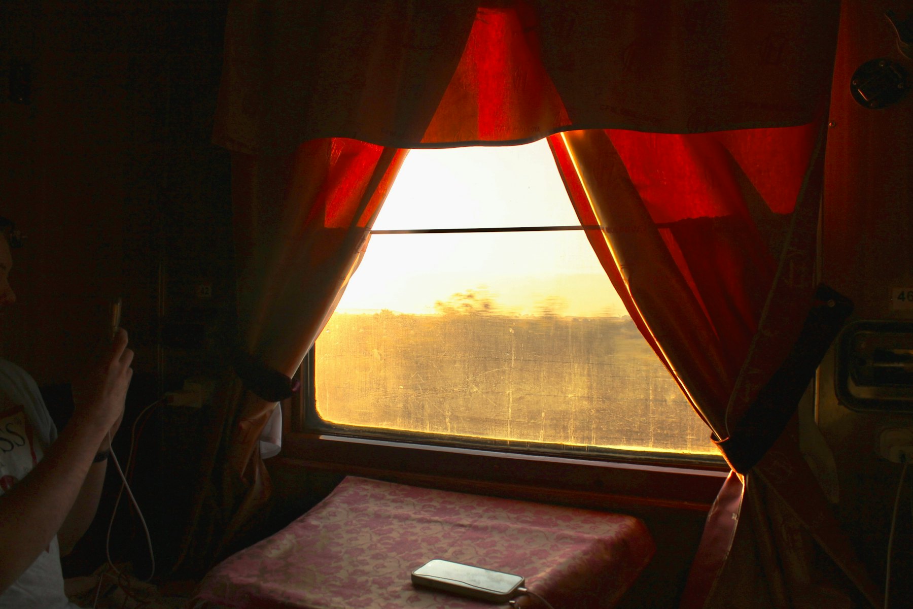 Golden sunrise light coming through a train window with red curtains