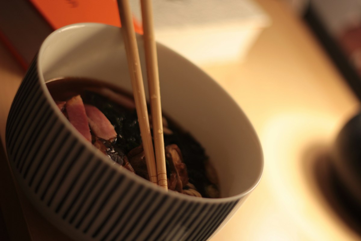 Chopsticks lifting dark noodles from a striped bowl