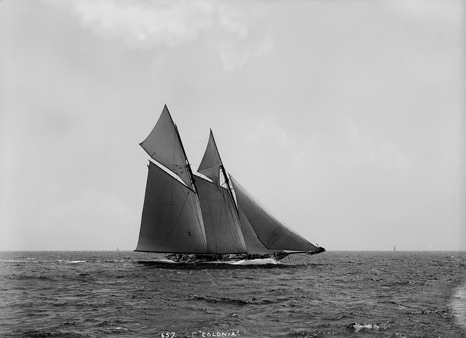 A dark-sailed schooner reaching under a lowering grey sky, black and white photograph