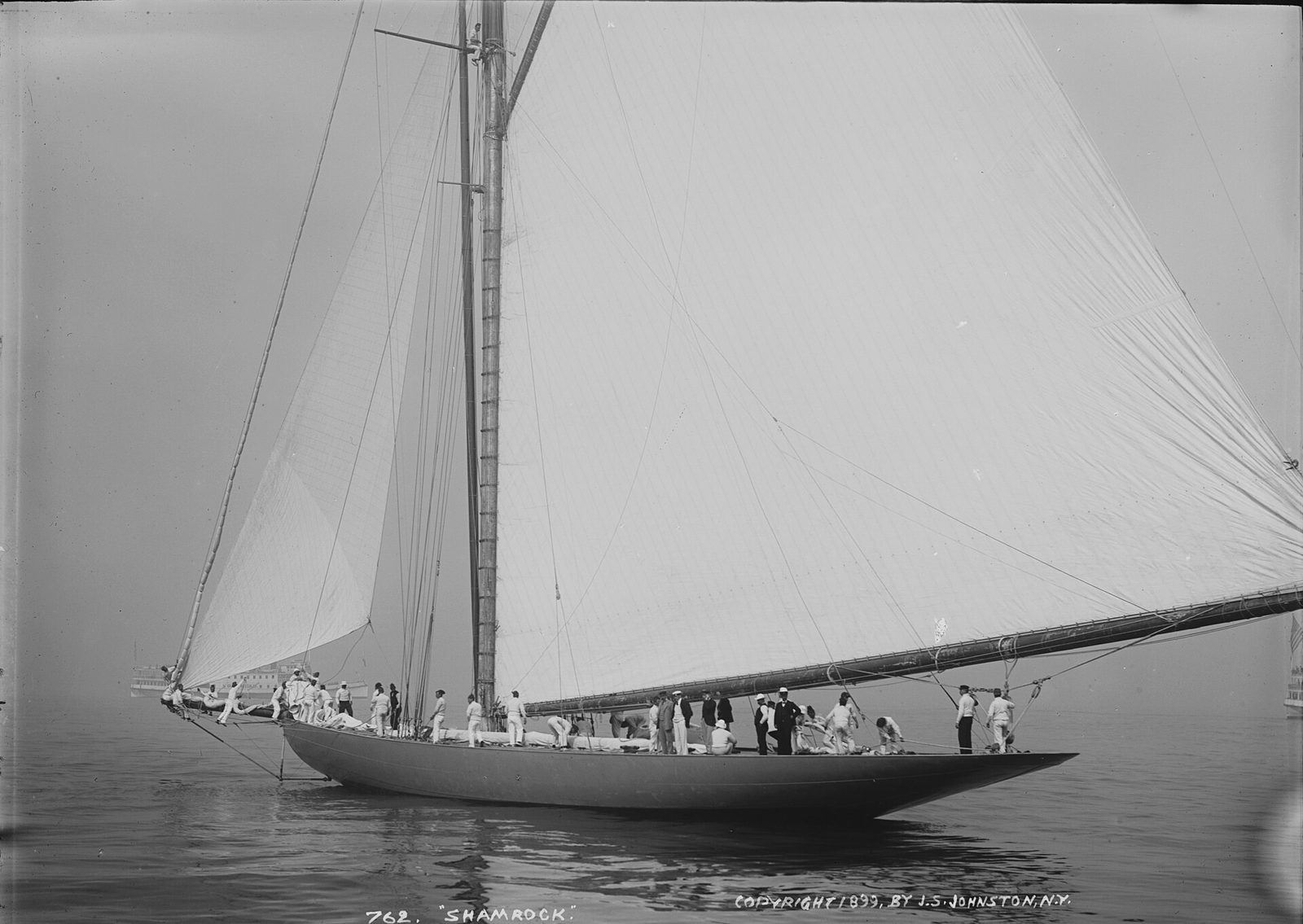 A white cutter heeling under full sail with her crew outboard, black and white photograph